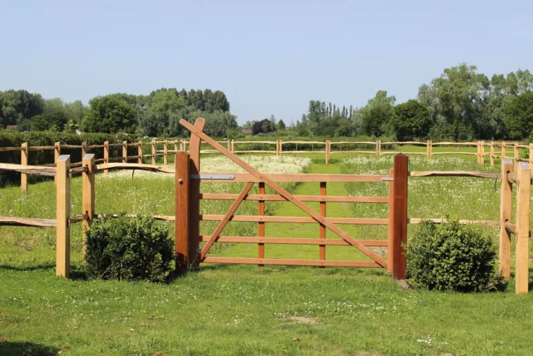 A wooden field gate with an arch connected to a wooden fence.