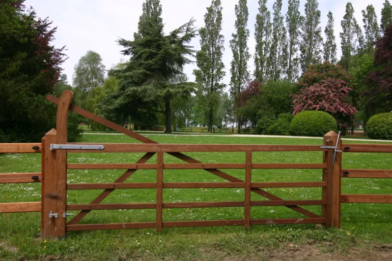 A wooden field gate with an arch connected to a wooden fence.