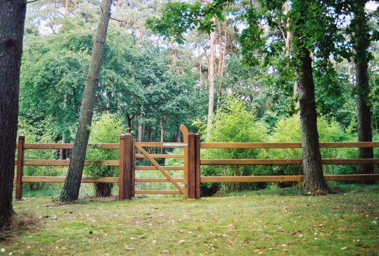 Einfaches Gartentor mit einem Bogen auf einer Seite, das an einem Holzzaun mit quadratischen Pfosten befestigt ist.