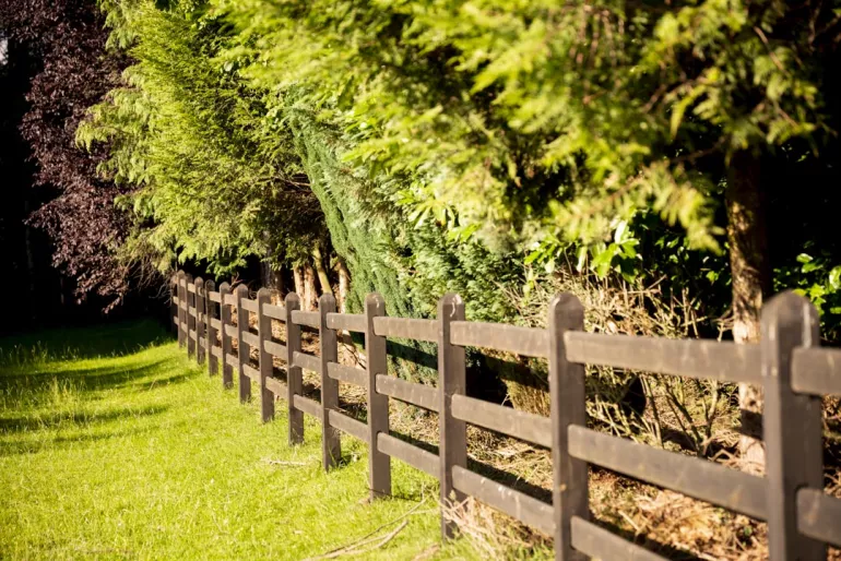 Une clôture en bois noir avec des poteaux carrés et 3 lisses entourant un champ