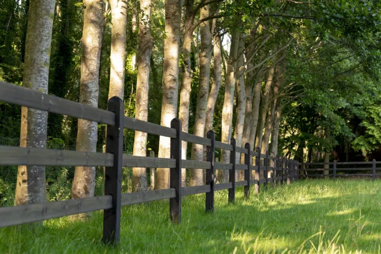 Une clôture en bois noir avec des poteaux carrés et 3 lisses entourant un champ
