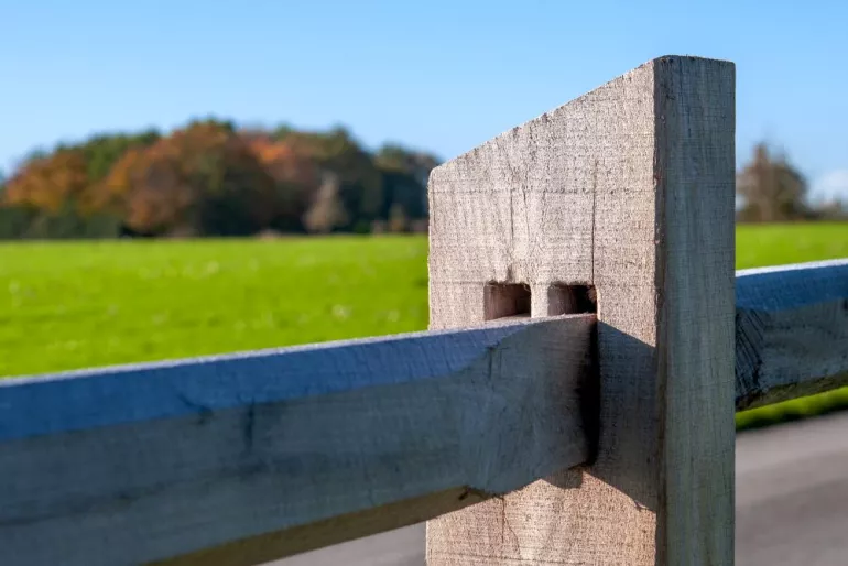Ein hölzernes Geländerbrett, das durch den Vierkantpfosten eines Zauns gleitet