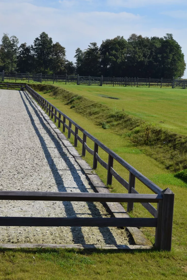 Clôture en bois à un rail et un rail supérieur continu entourant un manège pour chevaux