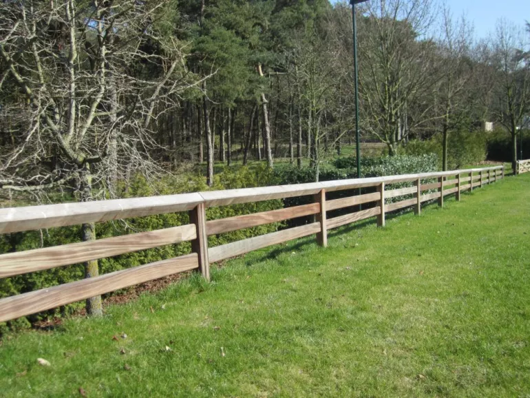 Une clôture en bois avec deux rails, des planches qui glissent à travers les poteaux et un rail supérieur continu.