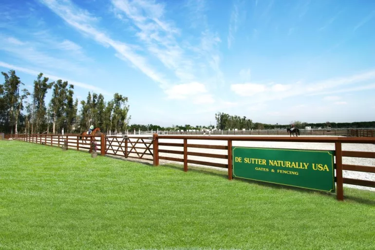 Un manège entouré d'une clôture en bois à 3 lisses et une lisse supérieure continue attachée à un portail en bois.
