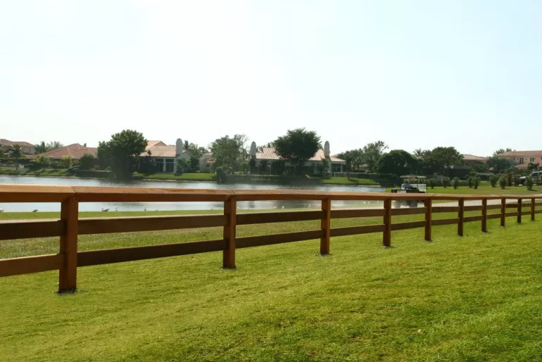 Une clôture en bois avec des poteaux carrés, deux lisses et une lisse supérieure continue sur un terrain de golf