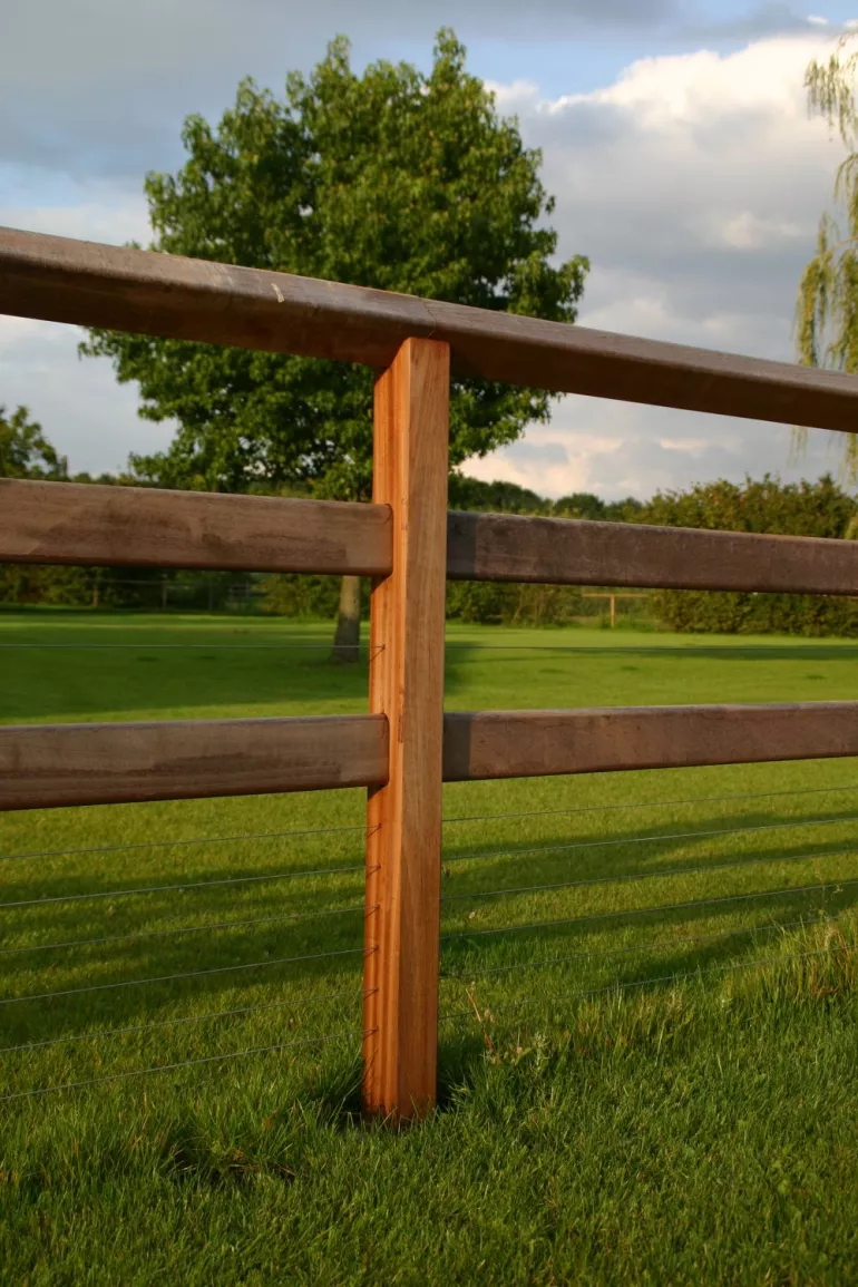 Le poteau carré en bois d'une clôture à deux lisses et une lisse supérieure continue.
