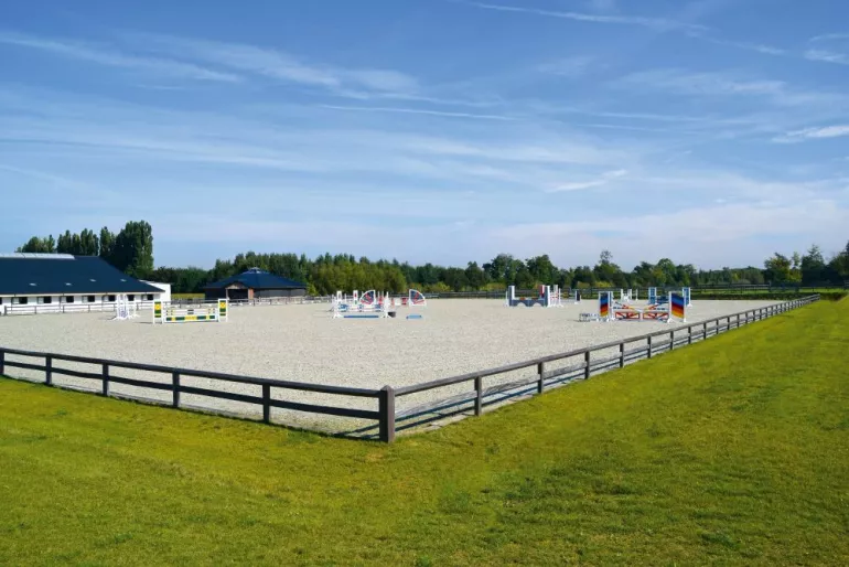 Une piste de saut d'obstacles entourée d'une clôture en bois avec une lisse et une lisse supérieure continue.
