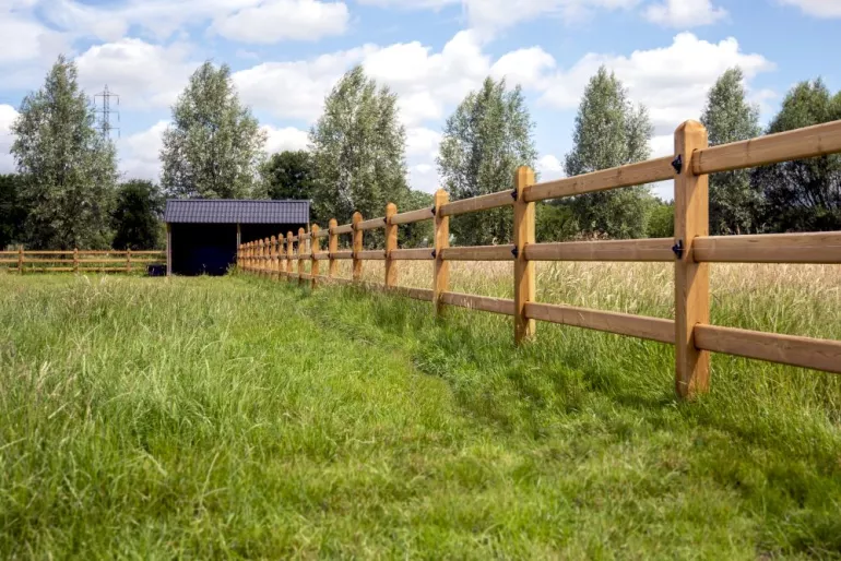Un double abri à chevaux en bois avec des tuiles noires relié à des clôtures en bois à 3 rails