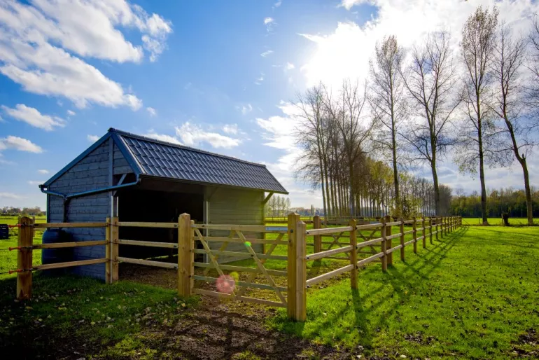 Ein doppelter Holzunterstand für Pferde und Freilandtiere mit einem Dach aus roten Ziegeln