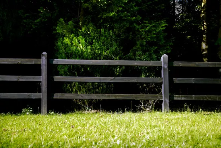 Ein schwarzer Holzzaun mit quadratischen Pfosten und 3 Stäben