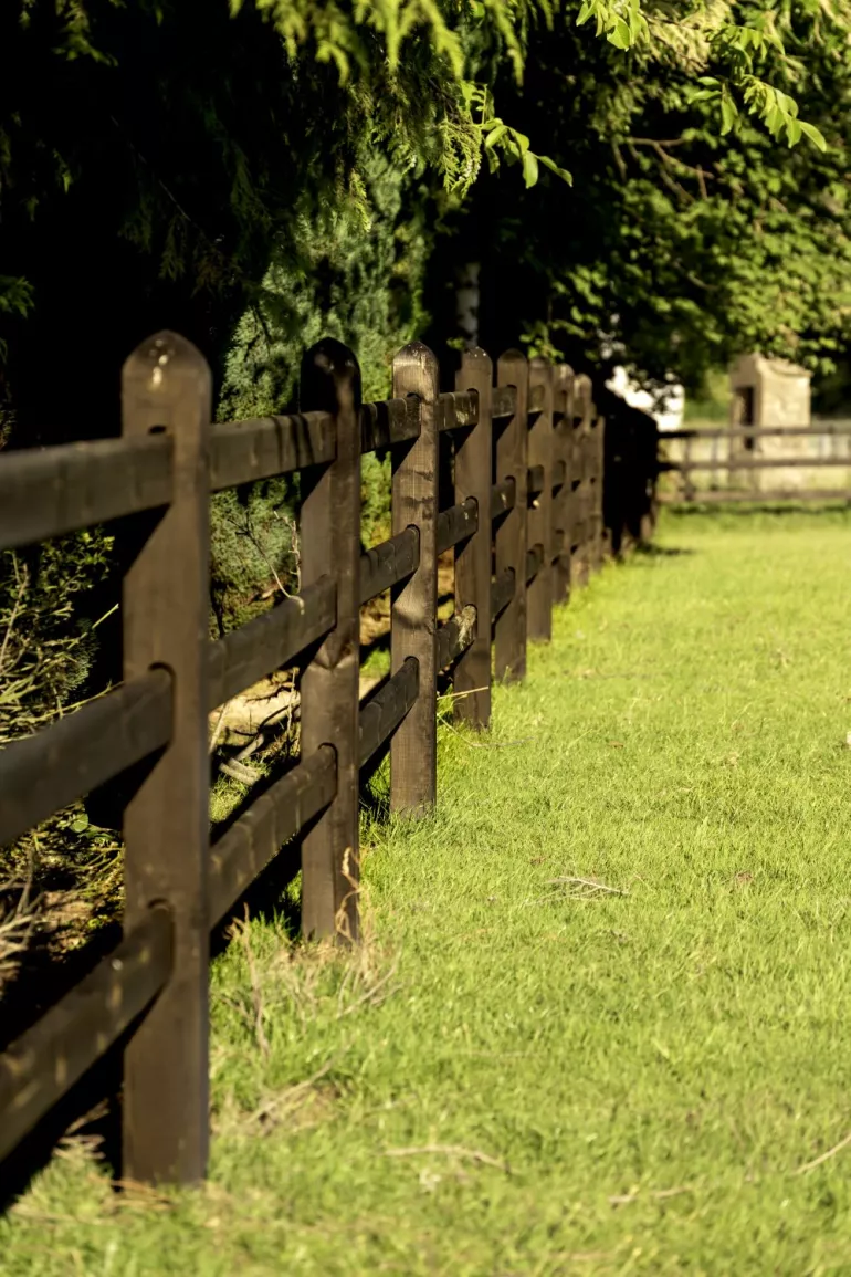 Ein schwarzer Holzzaun mit 3 Stäben, bei dem die Bretter durch die quadratischen Pfosten gleiten