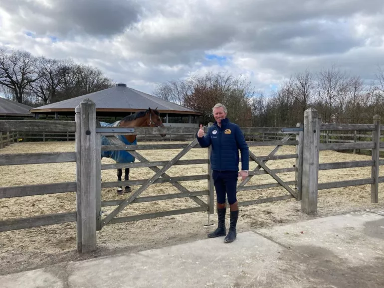 A horse in a riding arena enclosed with a double wooden gate attached to wooden fences with four rails
