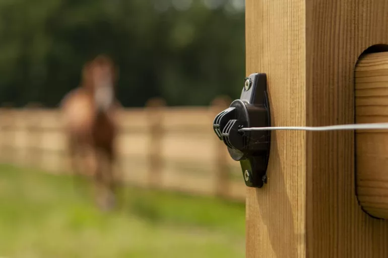 A close up to an electric wire attached to a wooden fence