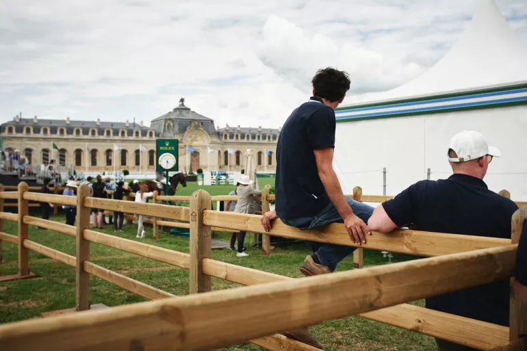 A person sitting on wooden fences with rails and square posts
