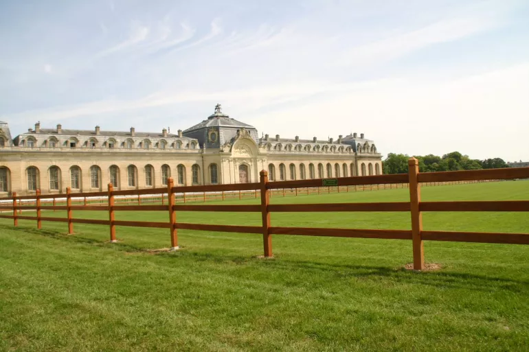 Clôtures en bois à 3 rails et poteaux carrés avec un sommet en forme de diamant entourant un grand champ.