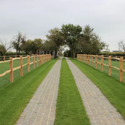 Un chemin entre des clôtures en châtaignier fendu avec 2 rails, des poteaux carrés et un grillage sur le dessus.