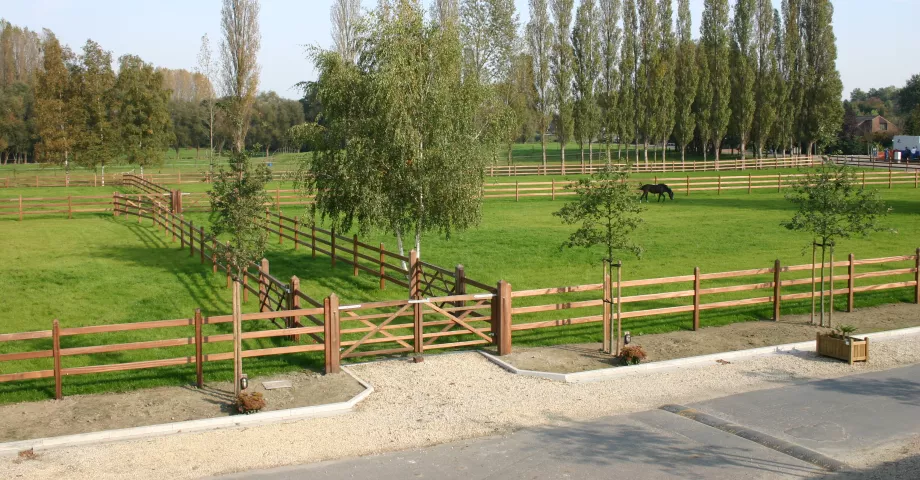 A double wooden gate gives access to a path bordered by numerous fields fenced by 3-sided wooden gates.