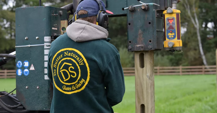 Un homme installe des clôtures en bois à l'aide d'une machine à vibrer les poteaux.