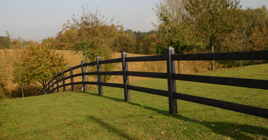 Een zwart houten omheining met vierkante palen en 3 rails op een veld
